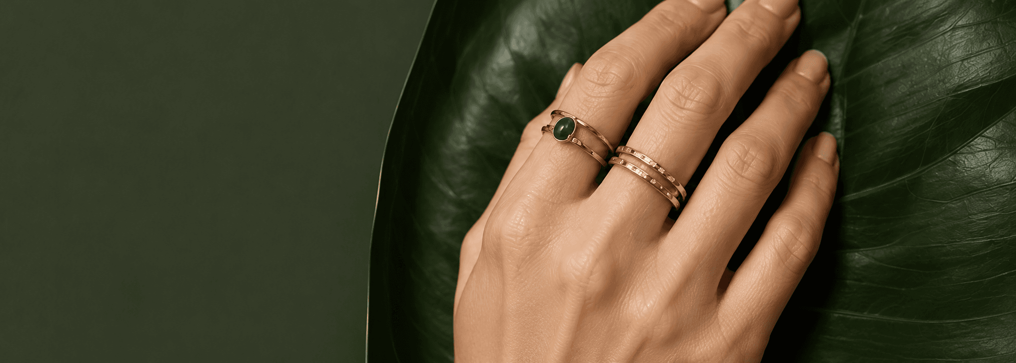 A hand wearing stacked Aniqas gold rings, resting on a leaf