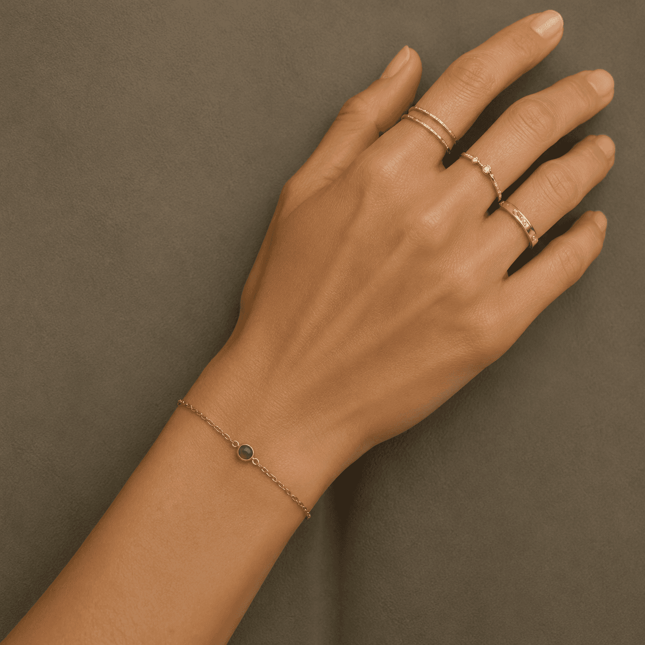 Hand wearing stacked gold rings and a fine green-stone bracelet