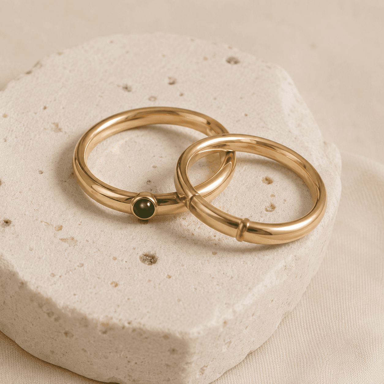Two gold rings resting on a travertine plinth in soft daylight